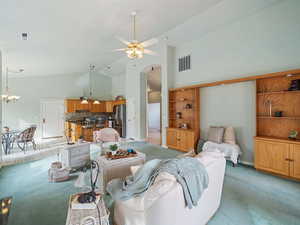 Carpeted living room with high vaulted ceiling and ceiling fan with notable chandelier