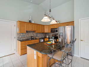 Kitchen with a kitchen island, appliances with stainless steel finishes, light tile patterned floors, high vaulted ceiling, and sink