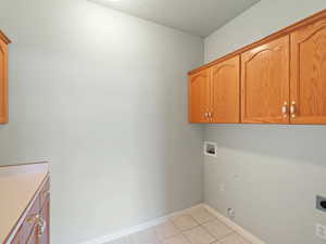 Laundry room featuring hookup for a washing machine, a textured ceiling, light tile patterned floors, cabinets, and electric dryer hookup