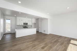 Kitchen with backsplash, stainless steel appliances, white cabinets, hardwood / wood-style floors, and an island with sink