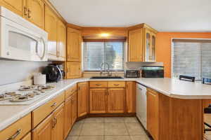 Kitchen with white appliances, light tile patterned floors, sink, a kitchen breakfast bar, and kitchen peninsula