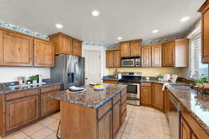 Kitchen with light tile patterned flooring, stainless steel appliances, a textured ceiling, sink, and a center island