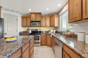 Kitchen with dark stone counters, appliances with stainless steel finishes, sink, and light tile patterned floors