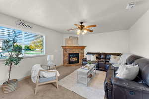 Living room with ceiling fan, a stone fireplace, a textured ceiling, and light carpet