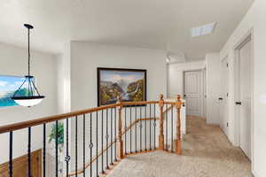 Hallway featuring a textured ceiling and light colored carpet