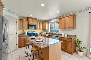 Kitchen with stainless steel appliances, a textured ceiling, stone countertops, a kitchen breakfast bar, and a center island