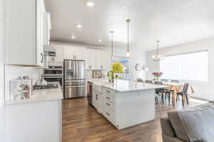 Kitchen with white cabinetry, sink, appliances with stainless steel finishes, a kitchen island with sink, and dark wood-type flooring