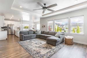 Living room with ceiling fan with notable chandelier, plenty of natural light, dark hardwood / wood-style floors, and a tray ceiling