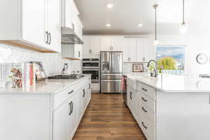 Kitchen featuring stainless steel appliances, white cabinetry, pendant lighting, dark wood-type flooring, and wall chimney exhaust hood