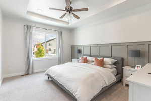 Bedroom with light colored carpet, ceiling fan, and a tray ceiling