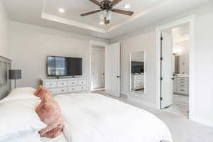 Carpeted bedroom with ceiling fan, connected bathroom, and a tray ceiling