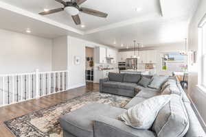 Living room with hardwood / wood-style floors, ceiling fan with notable chandelier, sink, and a tray ceiling