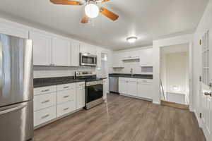 Kitchen with stainless steel appliances, light hardwood / wood-style floors, sink, white cabinets, and decorative backsplash