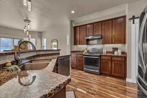 Kitchen with appliances with stainless steel finishes, a barn door, dark hardwood / wood-style floors, pendant lighting, and sink