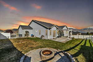 Back house at dusk with an outdoor fire pit, a pergola, a patio area, a mountain view, and a lawn