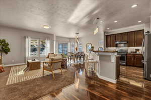 Kitchen with appliances with stainless steel finishes, a textured ceiling, decorative light fixtures, an island with sink, and dark wood-type flooring