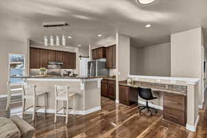 Kitchen with built in desk, a center island with sink, a kitchen bar, hanging light fixtures, and dark wood-type flooring