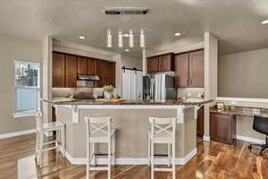 Kitchen featuring hardwood / wood-style flooring, a breakfast bar, decorative light fixtures, a barn door, and stainless steel fridge