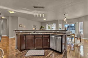 Kitchen featuring pendant lighting, a kitchen island with sink, stainless steel dishwasher, and dark hardwood / wood-style floors