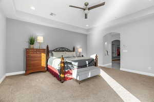 Carpeted bedroom with ceiling fan and a raised ceiling