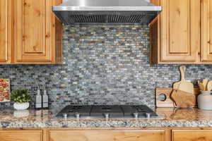 Kitchen featuring stainless steel gas cooktop, tasteful backsplash, and wall chimney range hood