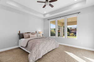 Bedroom featuring ceiling fan, a tray ceiling, and carpet