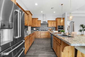 Kitchen with sink, a breakfast bar, appliances with stainless steel finishes, wall chimney exhaust hood, and hanging light fixtures