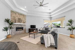 Carpeted living room featuring a fireplace, ceiling fan, and a raised ceiling