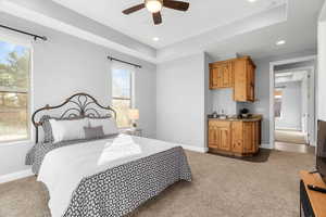 Carpeted bedroom featuring ceiling fan and a raised ceiling