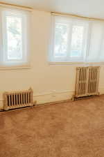 Empty room with radiator, carpet, and a healthy amount of sunlight