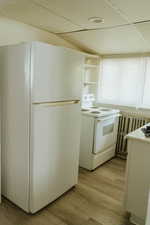 Kitchen featuring white appliances, light hardwood / wood-style flooring, and a drop ceiling