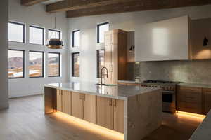 Kitchen featuring beamed ceiling, sink, light stone countertops, light hardwood / wood-style flooring, and stainless steel range