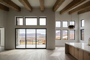 Unfurnished living room with a wealth of natural light, a mountain view, beam ceiling, and light hardwood / wood-style floors