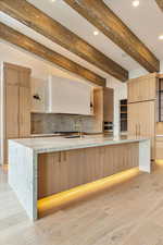 Kitchen with oven, decorative backsplash, a large island with sink, and beam ceiling