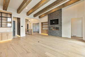 Unfurnished living room featuring a fireplace, beamed ceiling, and light hardwood / wood-style flooring