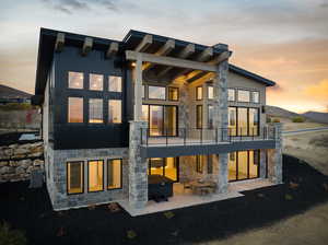 Back house at dusk with a mountain view, a balcony, and a patio area