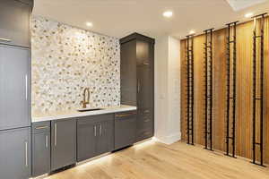 Bar with dishwasher, tasteful backsplash, light wood-type flooring, and sink