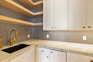 Kitchen with light stone countertops, white cabinetry, sink, and tasteful backsplash