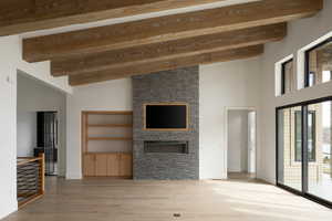 Unfurnished living room with wood-type flooring, a stone fireplace, and lofted ceiling with beams