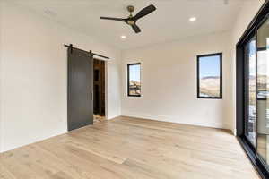 Spare room with a barn door, ceiling fan, and light wood-type flooring