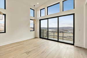 Empty room with a wealth of natural light, a high ceiling, a mountain view, and light hardwood / wood-style flooring