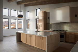 Kitchen with light brown cabinets, sink, stainless steel range, beamed ceiling, and light hardwood / wood-style flooring