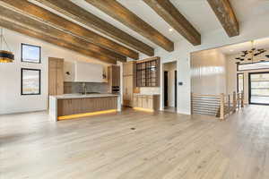 Unfurnished living room with light wood-type flooring, lofted ceiling with beams, and sink