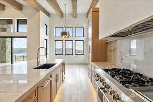 Kitchen with light hardwood / wood-style floors, high end stainless steel range oven, sink, light stone countertops, and decorative light fixtures