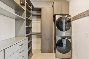 Laundry area with cabinets, stacked washer and dryer, and light tile patterned flooring