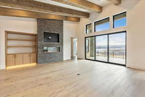 Unfurnished living room featuring a fireplace, light hardwood / wood-style floors, and beamed ceiling