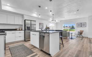 Kitchen with light hardwood / wood-style flooring, an island with sink, white cabinetry, appliances with stainless steel finishes, and decorative light fixtures