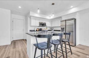 Kitchen with stainless steel appliances, light hardwood / wood-style floors, white cabinetry, a kitchen bar, and decorative light fixtures