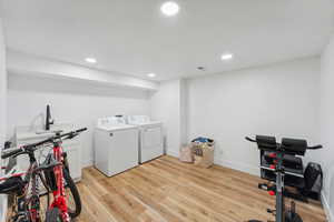 Washroom with light wood-type flooring and washing machine and dryer