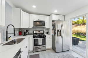 Kitchen featuring white cabinetry, sink, appliances with stainless steel finishes, tasteful backsplash, and light stone countertops